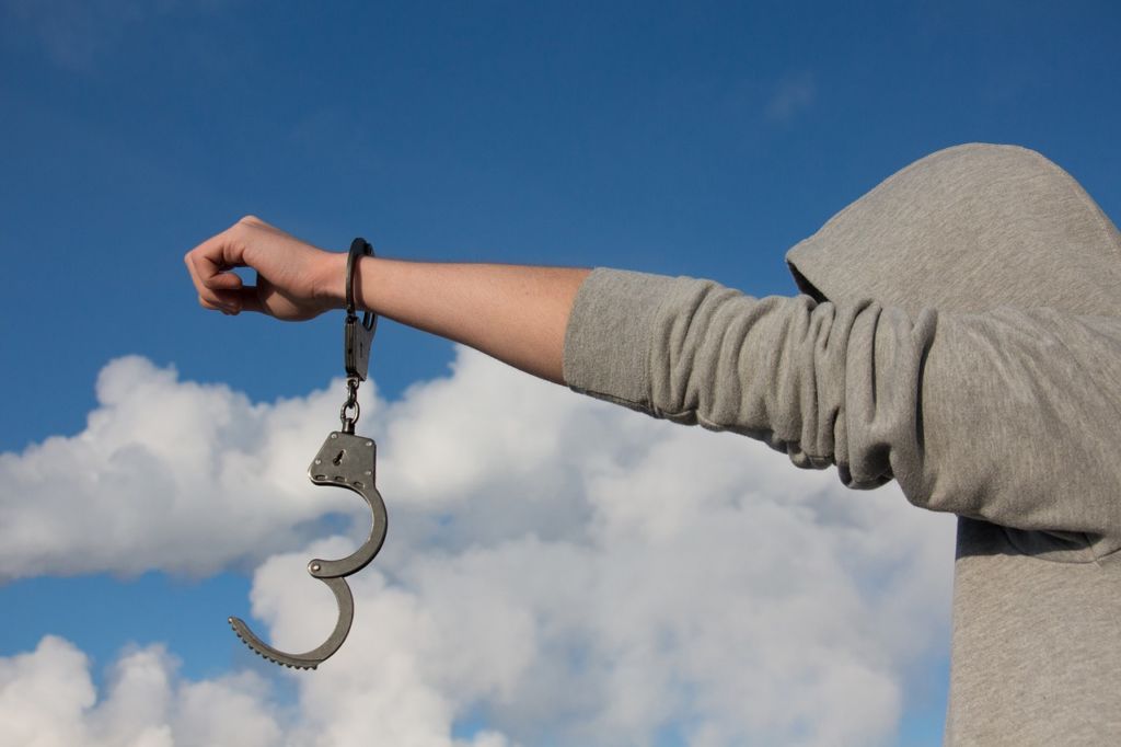 Man needing criminal defense holds up arm with handcuff dangling.